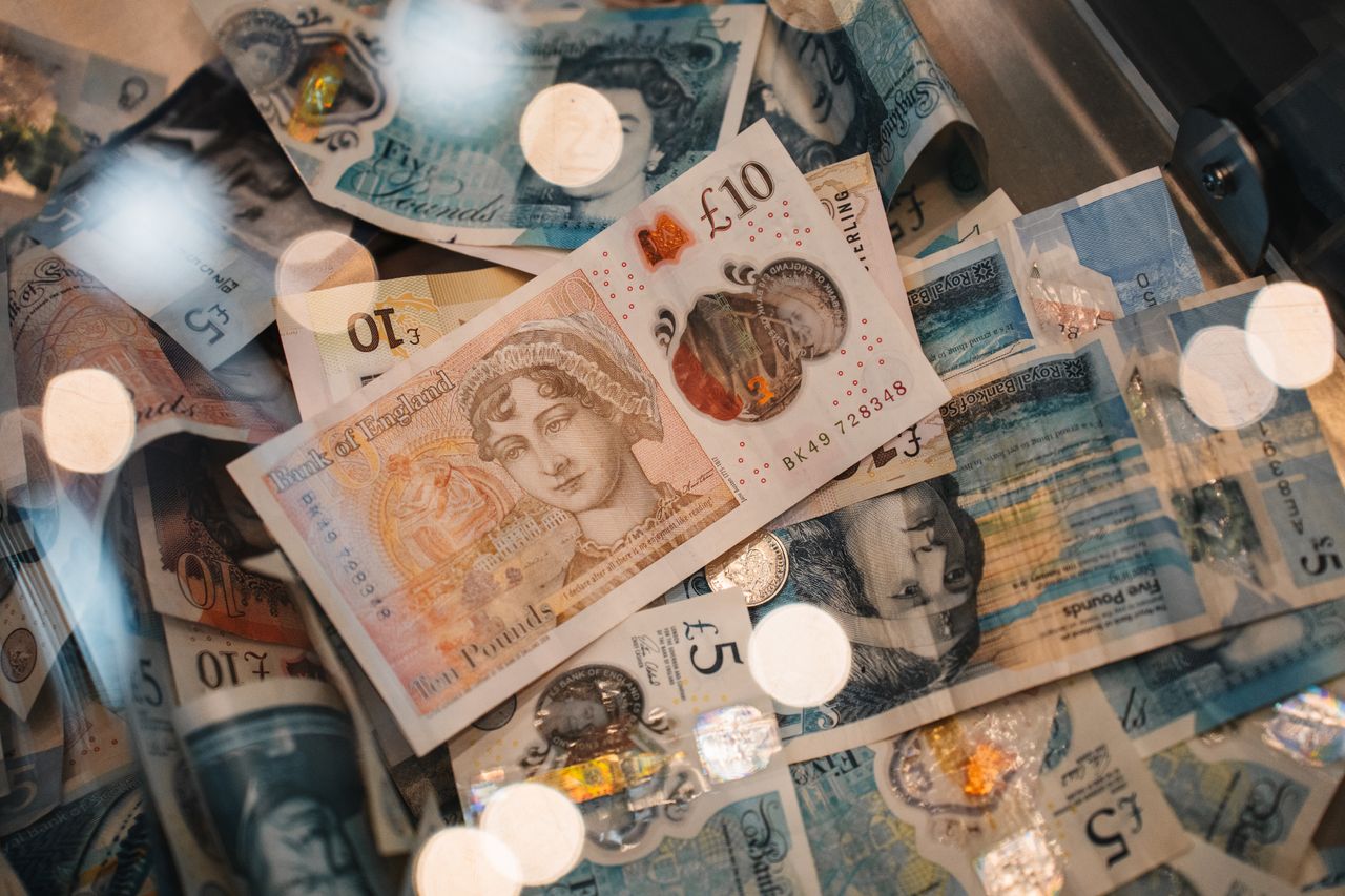 A detailed view of British £5 and £10 pound sterling notes with coins, featuring warm bokeh effects.